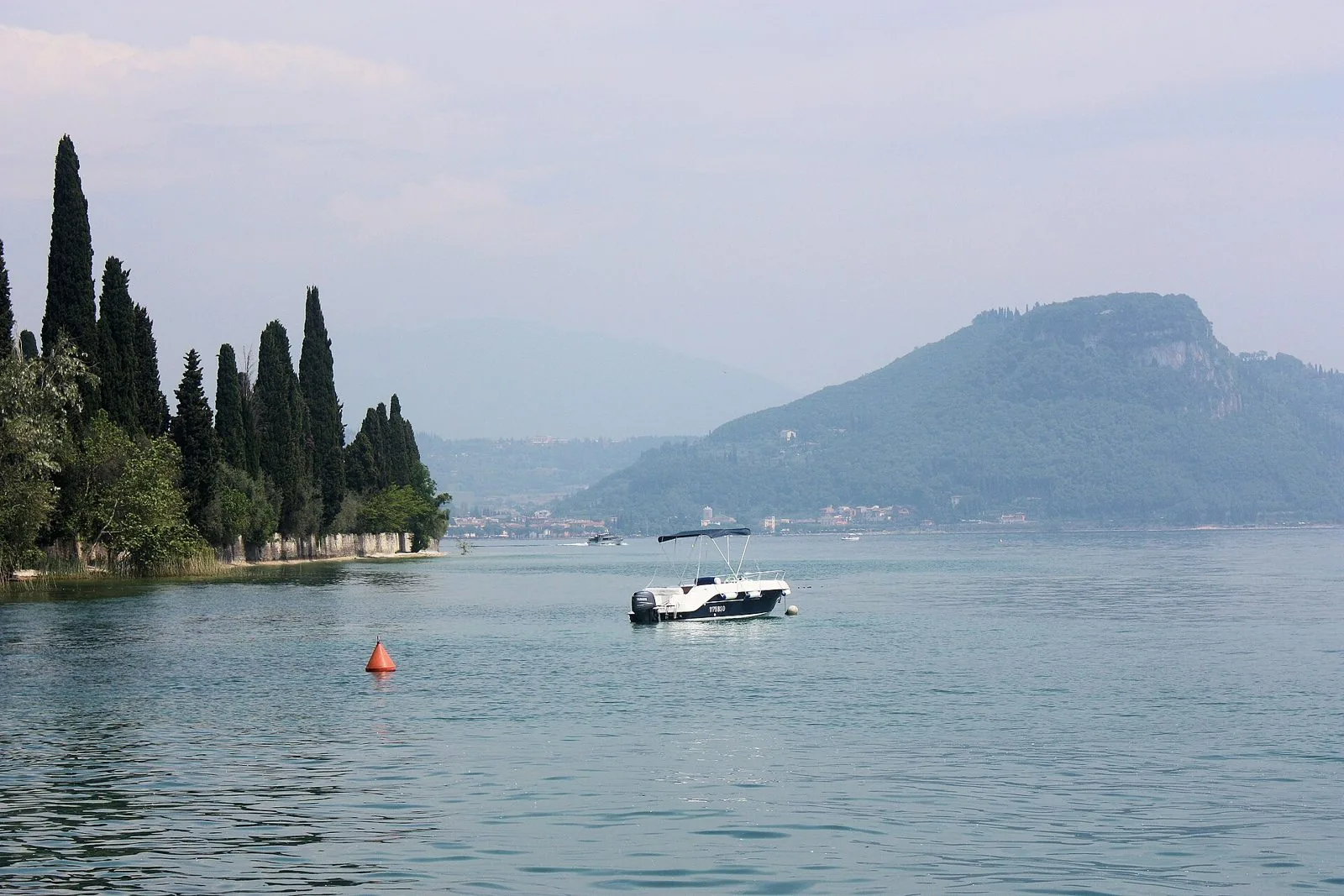 I cipressi di Punta San Vigilio sul lago e, sullo sfondo, il promontorio della Rocca di Garda
